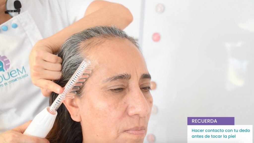 Cosmetóloga aplicando un tratamiento de alta frecuencia en el cuero cabelludo de una clienta.