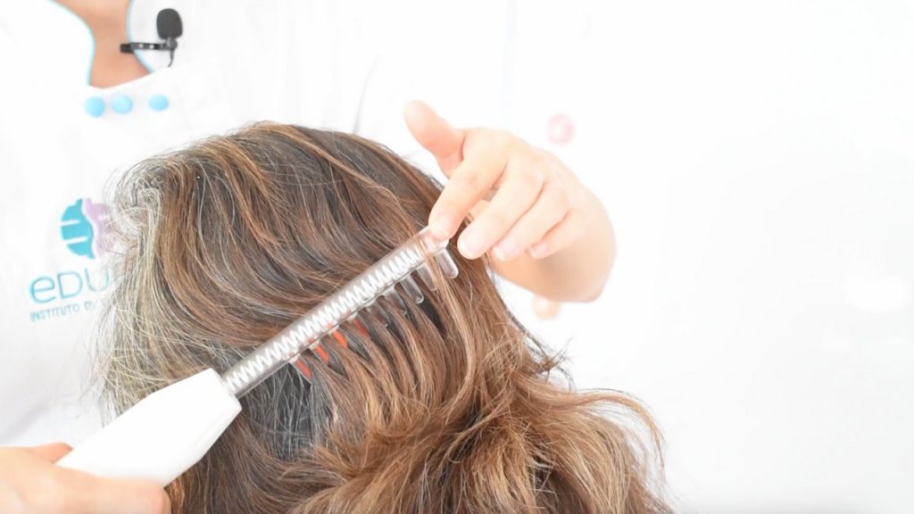 Mujer con el cabello seco y limpio recibiendo un tratamiento anticaída con aparato de alta frecuencia.