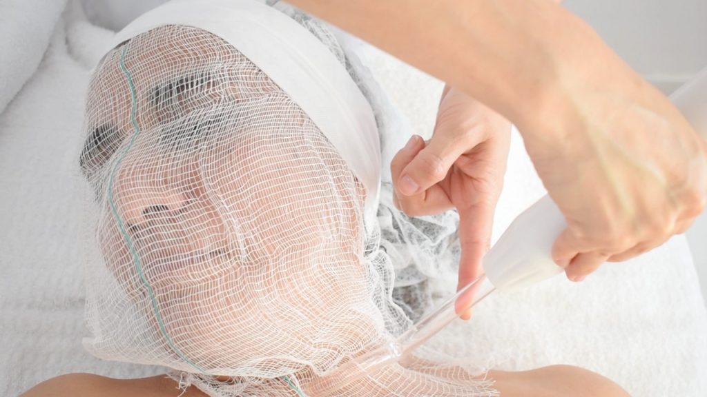 Cosmetóloga girando con delicadeza la cabeza de la clienta para continuar la aplicación de alta frecuencia facial.