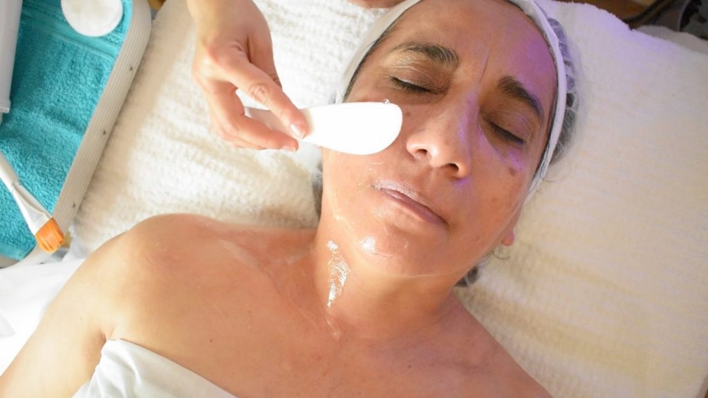 Cosmetóloga aplicando gel conductor en el rostro de la clienta antes de iniciar la radiofrecuencia facial.