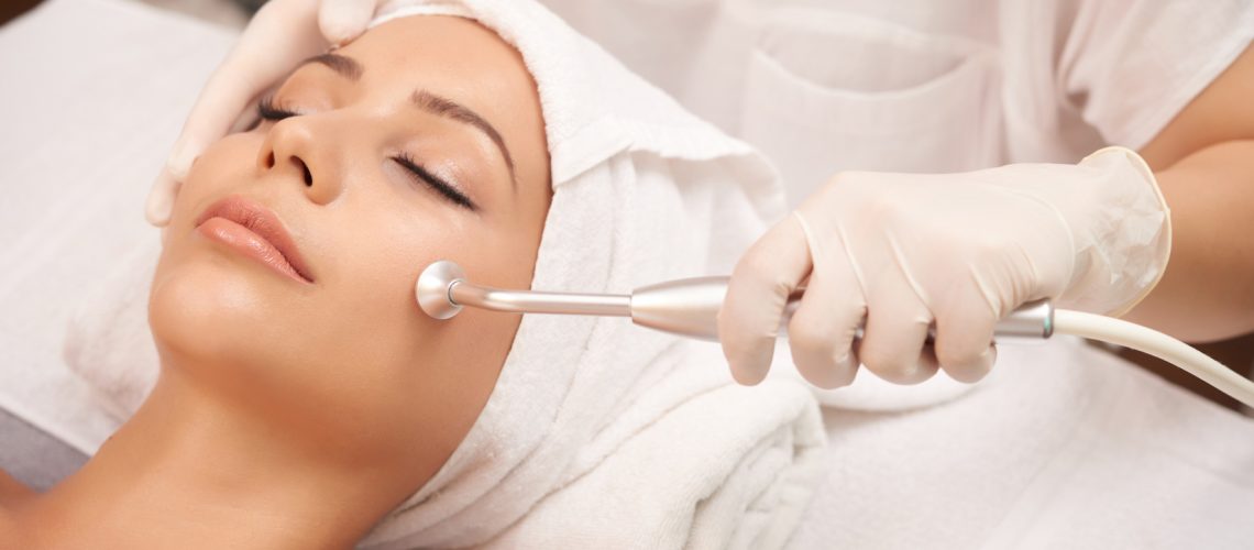 Cosmetologist using microdermabrasion machine for peeling, view from above